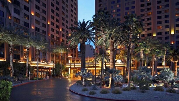 Un hotel con un viale curvo, palme e finestre illuminate.