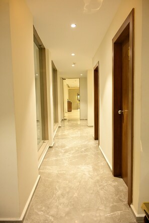 A hallway with a marble floor, wooden doors, and glass walls.