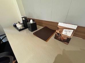 Mostrador de hotel con cafetera, caja de pañuelos y un cartel que dice 'Para cualquier asistencia'.