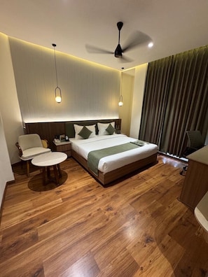 A hotel room with a bed, bedside table, chair, and a ceiling fan. - Trevon Hotel Gujrat Centrale (Ranchi)