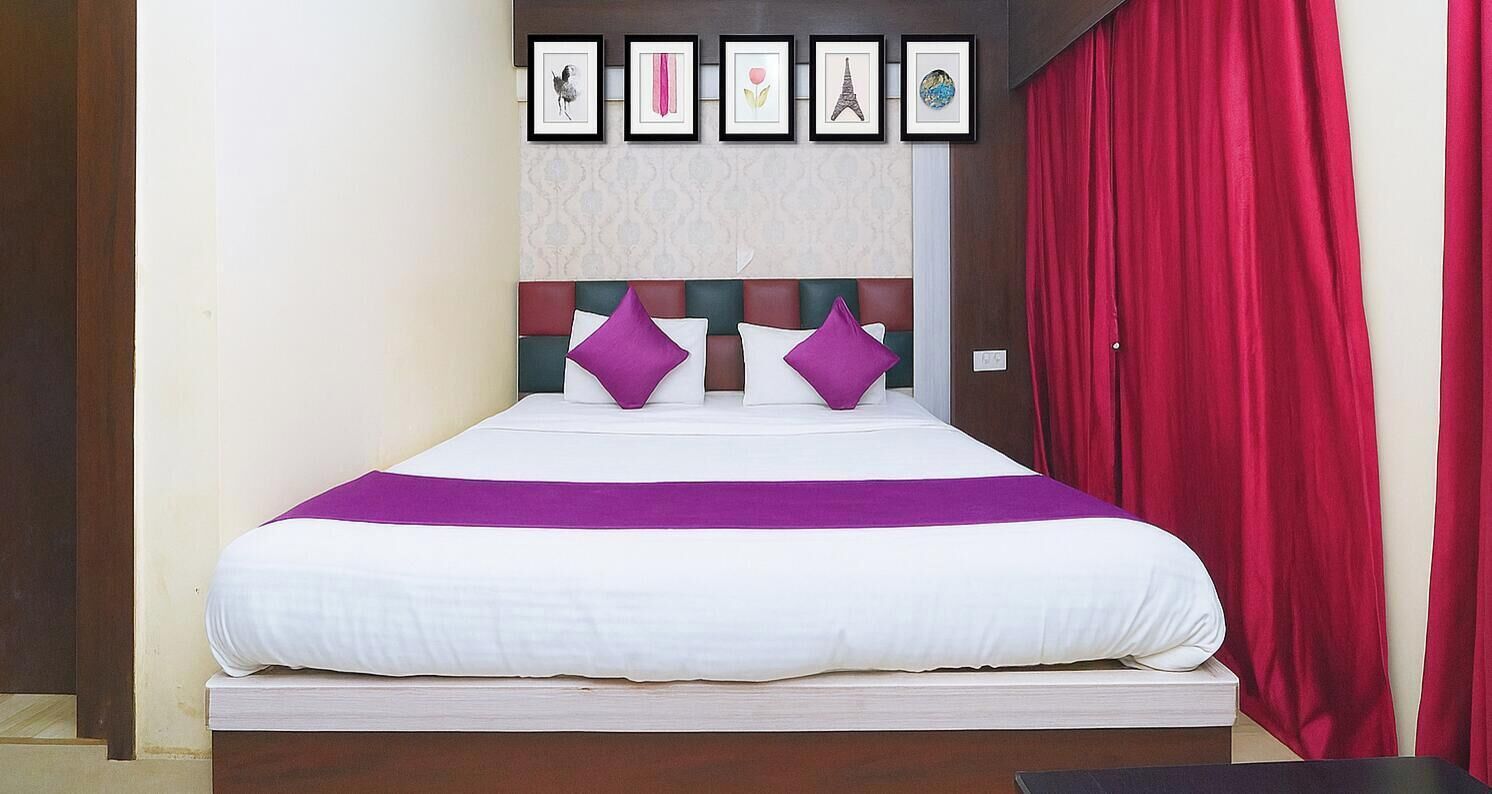 Un letto con una coperta bianca e viola, una testiera con motivo geometrico e una tenda rossa.