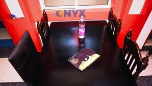 A black table with a bottle and a menu in front of a window with the sign 'ONYX DESTINATIONS'.