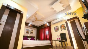 A hotel room with a bed, a desk, a chair, a ceiling fan, and a wall-mounted air conditioner.