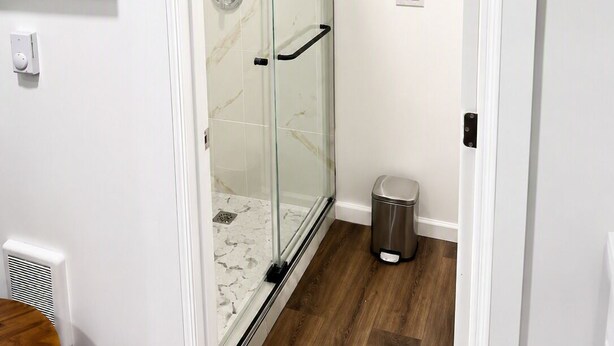A modern bathroom with a glass shower enclosure, a toilet, and a trash bin.