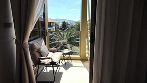 Ein Balkon mit Blick auf Gebäude und Palmen, ein Stuhl und ein Tisch.
