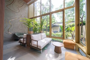 A modern interior with a sofa, a round table, and a window with a view of greenery. - Cozy 1-bedroom apartment in Laguna Beachside (Thalang District)