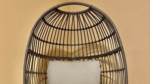 Una silla de mimbre con asiento y respaldo acolchados, dos cojines decorativos y patas de metal.