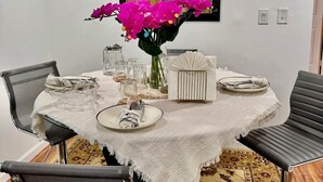 Un comedor con una mesa redonda, sillas, un florero con flores y un reloj en la pared.