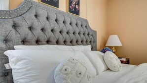 Una cama con cabecera capitonada, ropa de cama blanca y una mesita de noche con lámpara y objetos decorativos.