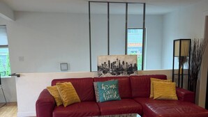 Uma sala de estar moderna com um sofá de couro vermelho, uma mesa de centro de vidro e uma pintura com vista para a cidade na parede.