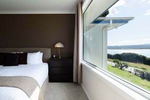Une chambre à coucher comprenant un lit, une table de chevet, une lampe et une grande fenêtre donnant sur un paysage.