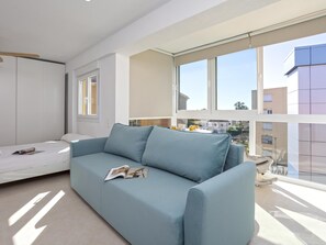 Ein modernes Wohnzimmer mit einem hellblauen Sofa, einem kleinen Tisch mit einer Zeitschrift und großen Fenstern mit Blick auf die Nachbarschaft.