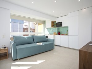 Ein modernes Wohnzimmer mit einer Couch, einer Küchenzeile und Blick ins Freie.