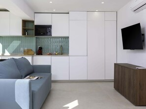 Eine moderne Küche mit integriertem Mikrowellenherd, einem an der Wand befestigten Fernseher und einem grauen Sofa im Wohnbereich.