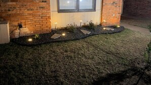 Fachada de tijolos com uma janela, um caminho iluminado e um pequeno jardim.