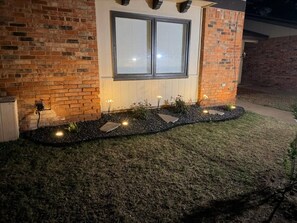 A brick exterior with a window, a pathway with lights, and a small garden area.