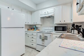 Una cocina moderna con armarios blancos, un refrigerador de acero inoxidable, un microondas y un lavamanos.