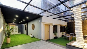 A spacious indoor area with a glass ceiling, artificial grass, and a stone pillar. - Chembur Homeotel - Gagal Home (Mumbai)