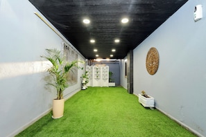 A narrow hallway with artificial green grass, white walls, and a black ceiling with recessed lighting.
