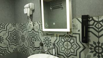 A bathroom with a white sink, a mirror with a light, patterned tiles, and a hairdryer on the wall.