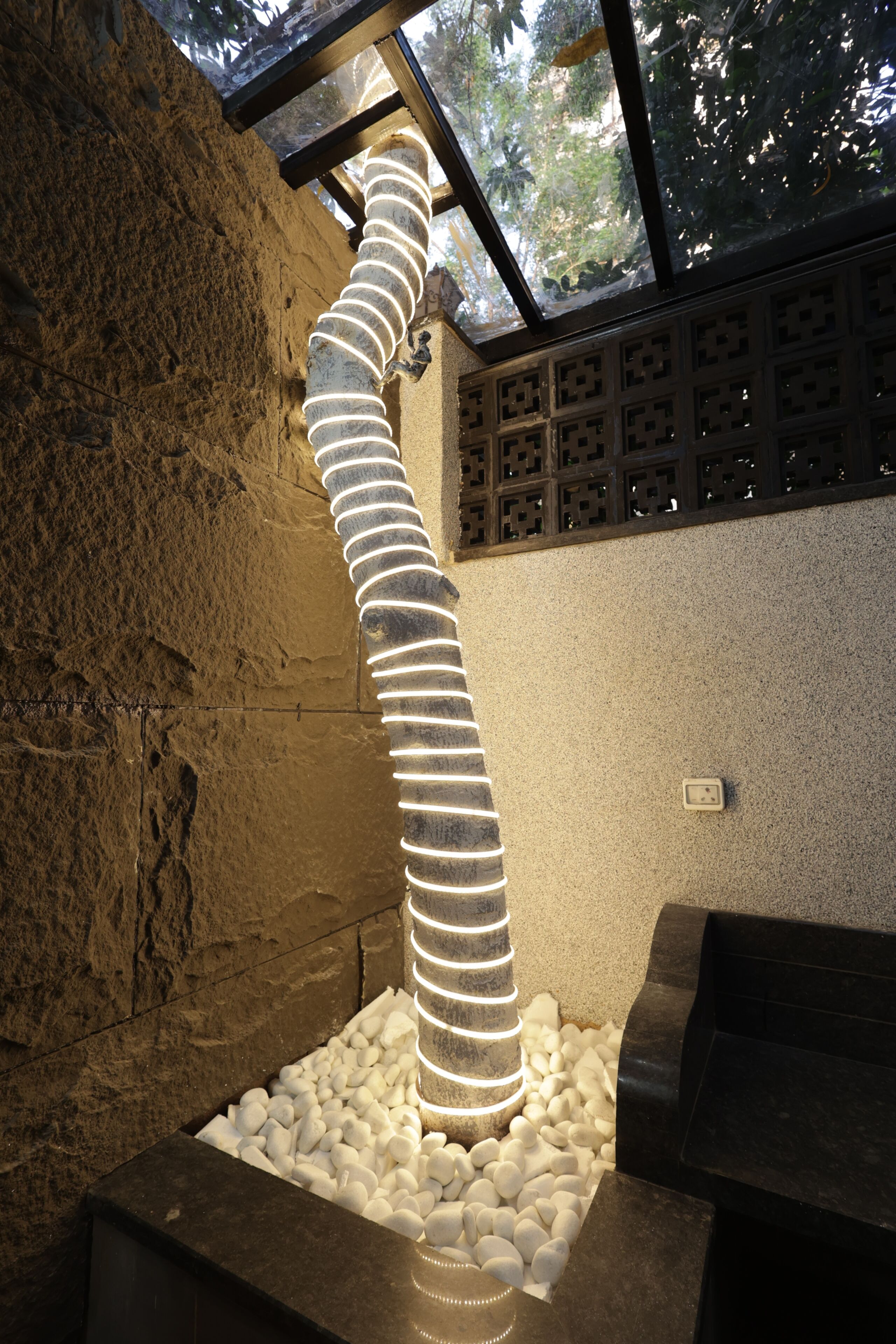 Una lámpara espiral en una habitación de paredes de piedra, con vistas a árboles a través de un techo de vidrio.