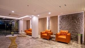 Un vestíbulo moderno con suelo de mármol, dos sillones naranjas, una mesita redonda y una columna alta.