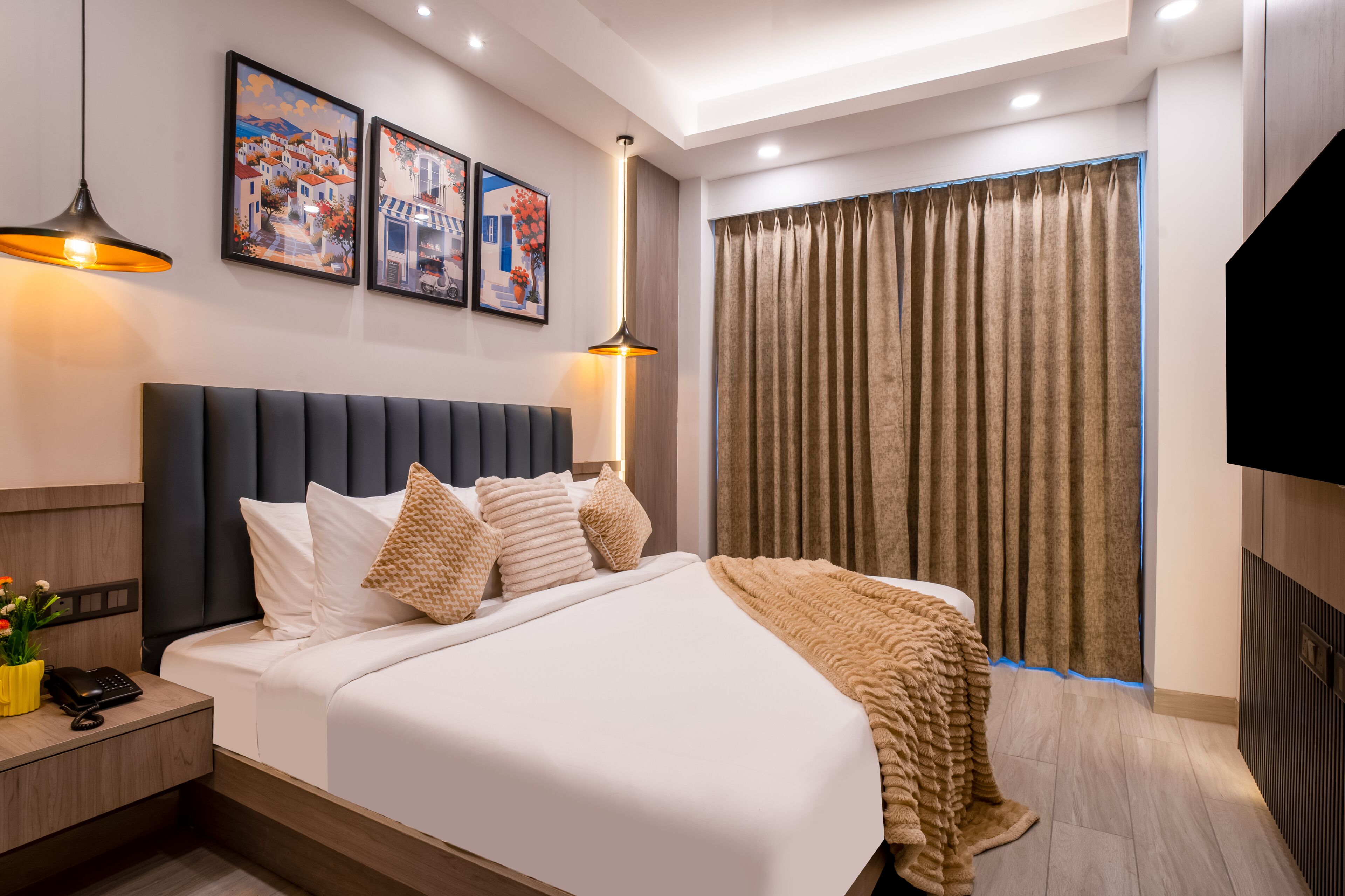 A hotel room with a bed, bedside table, lamp, artwork, curtains, and a TV.