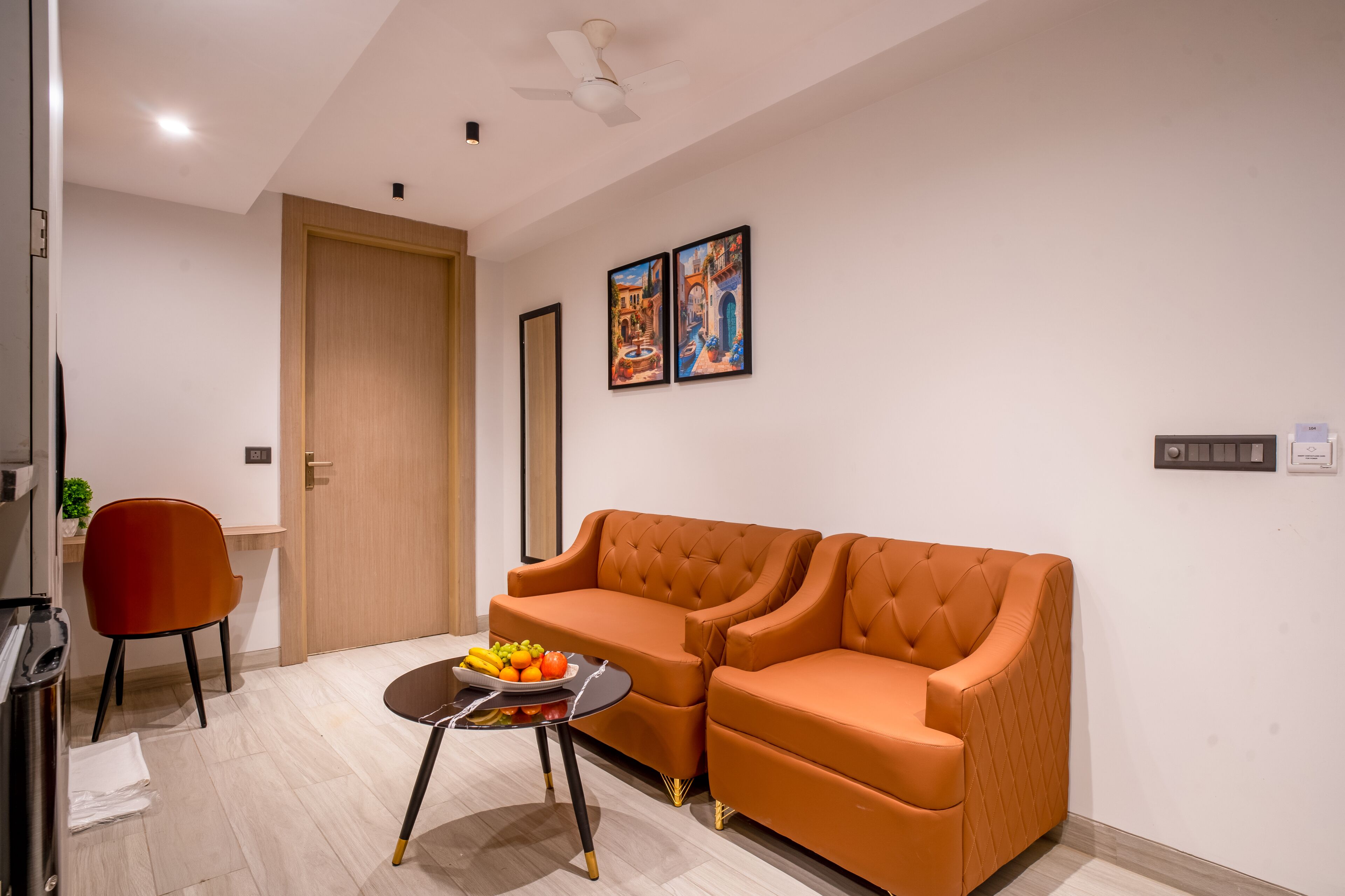 A modern living room with a sofa, a small table with fruit, a red chair, and a ceiling fan.
