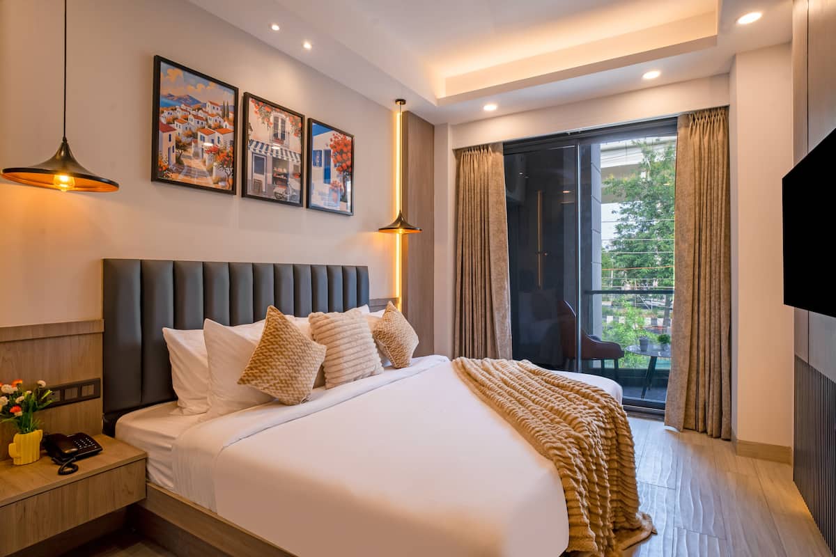 Habitació d'hotel moderna amb un llit gran, una tauleta de nit, un escriptori i un balcó amb cortines.