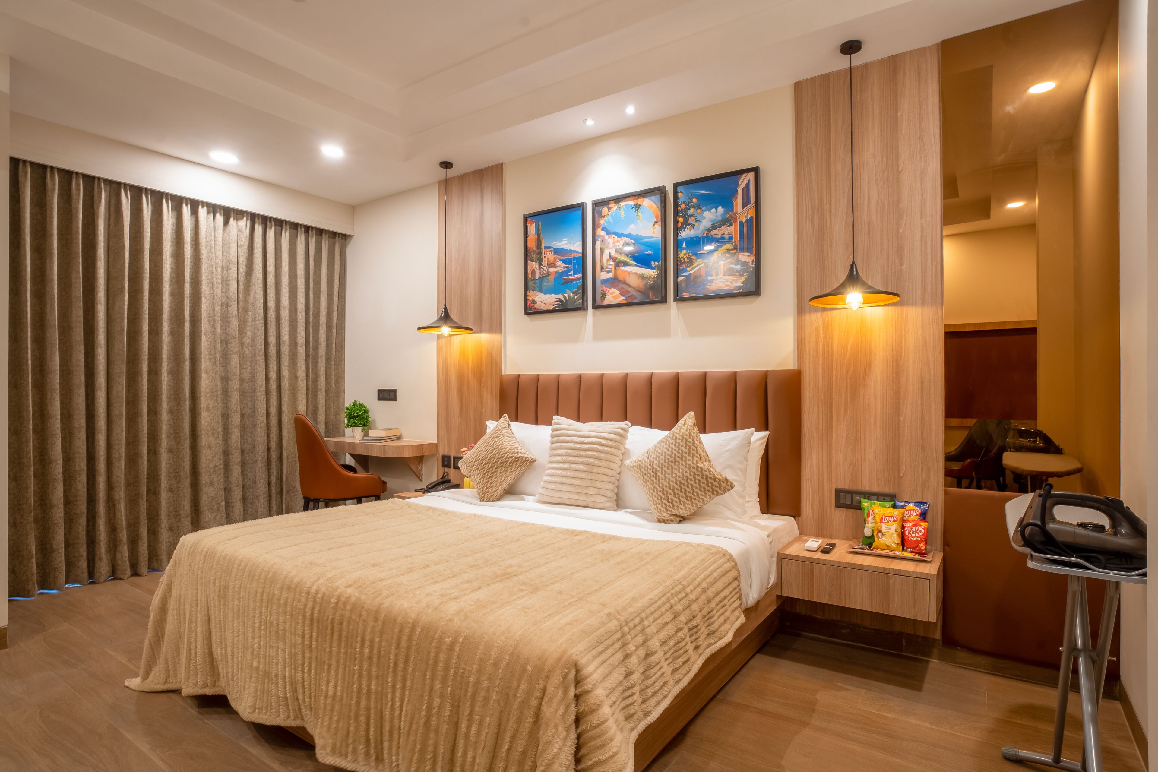 A modern hotel room with a large bed, a desk, a chair, and a small table with snacks.