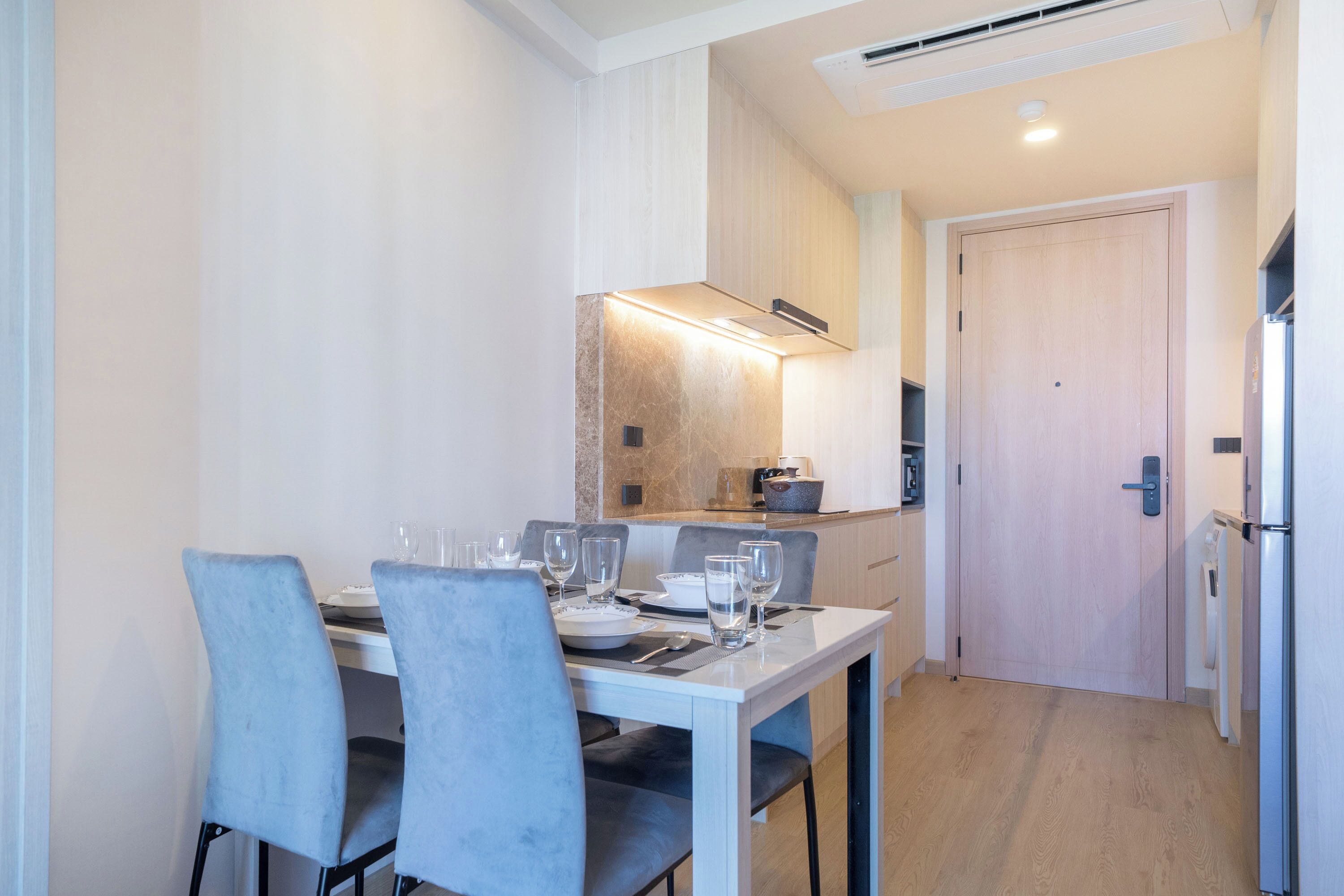 Een eetgedeelte met een tafel voor vier personen, stoelen, een keuken op de achtergrond en een deur.
