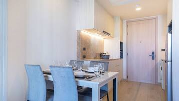 Een eetgedeelte met een tafel voor vier personen, stoelen, een keuken op de achtergrond en een deur.
