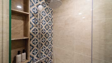 Een douche met een geometrisch tegelpatroon, een handdouche en twee flessen op een plank.