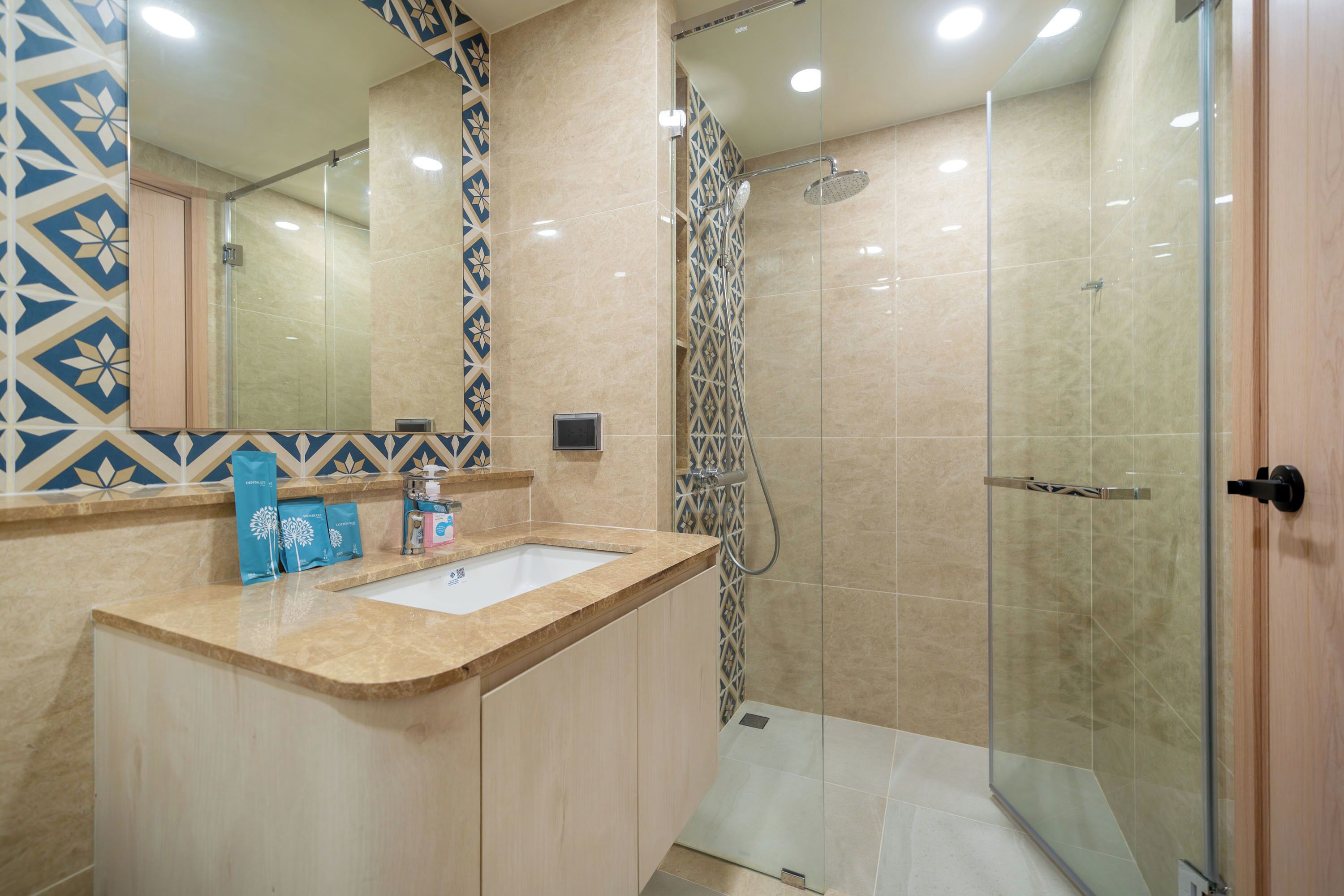 Un baño moderno con cabina de ducha de vidrio, lavamanos con encimera color beige y azulejos con diseño en la pared.