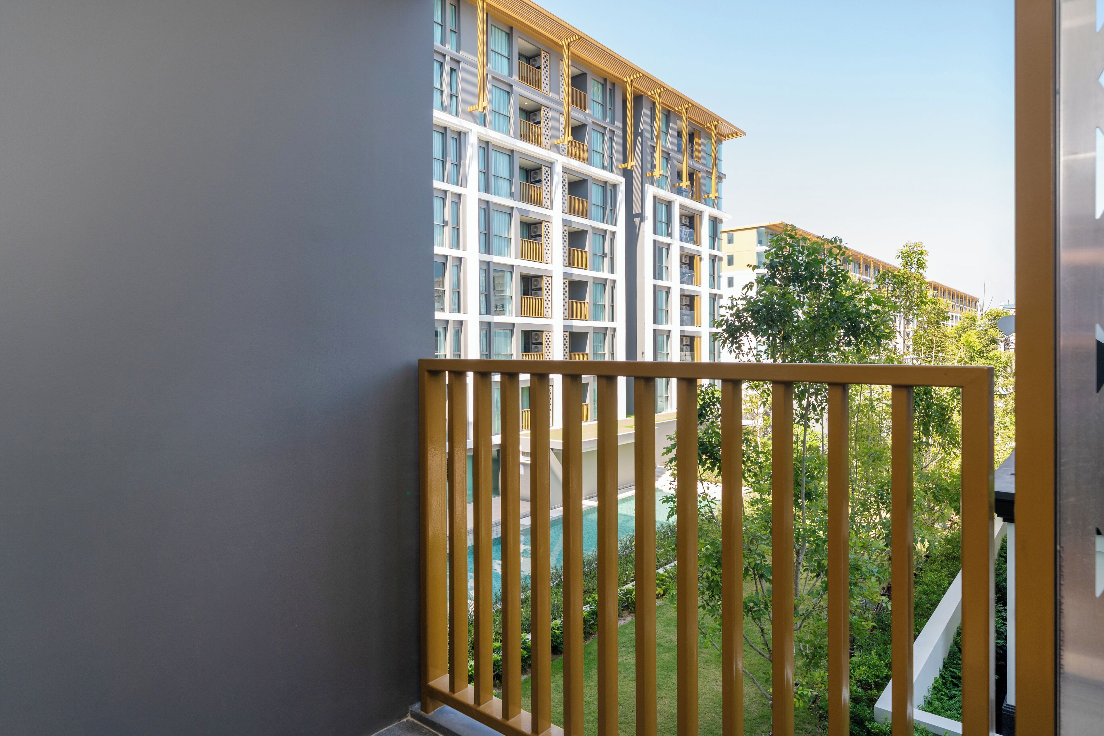 A multi-story building with balconies, a pool, and a view of greenery.