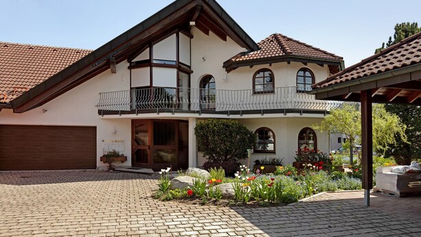 Una casa de dos pisos con balcón, garaje y jardín lleno de flores.