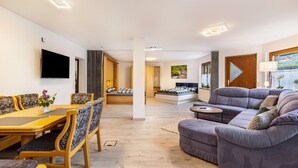 Una sala moderna con un sofá, una mesa de comedor con sillas, un televisor de pantalla plana montado en la pared y una cama con vistas a un jardín.