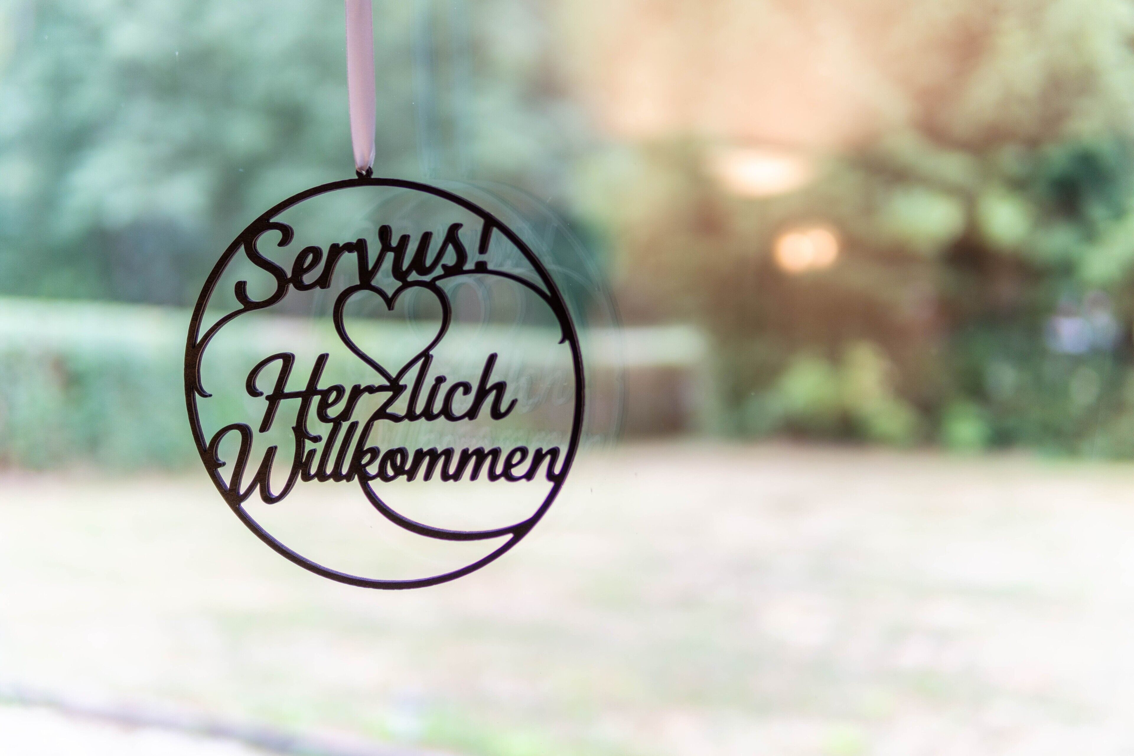 Un panneau circulaire portant l’inscription « Servus ! Herzlichen Willkommen » et suspendu à une corde.