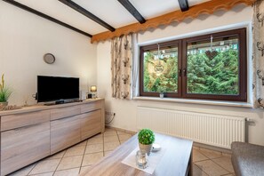 Ein modernes Wohnzimmer mit Flachbildfernseher, Holzschrank und Fenster mit Blick auf Grünflächen.
