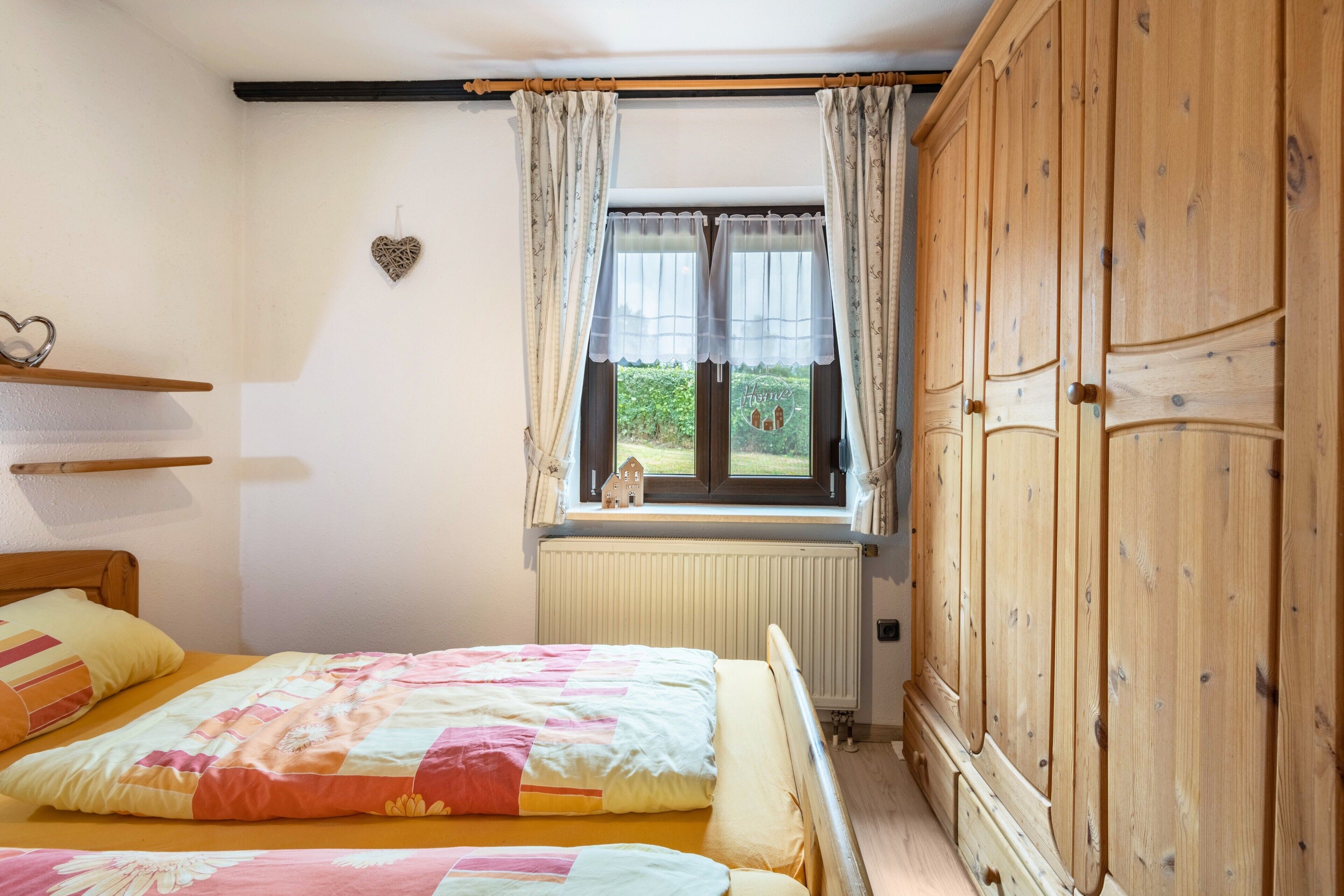 Ein Schlafzimmer mit zwei Betten, einem Fenster mit Vorhängen, einem Heizkörper und einem Holzschrank.