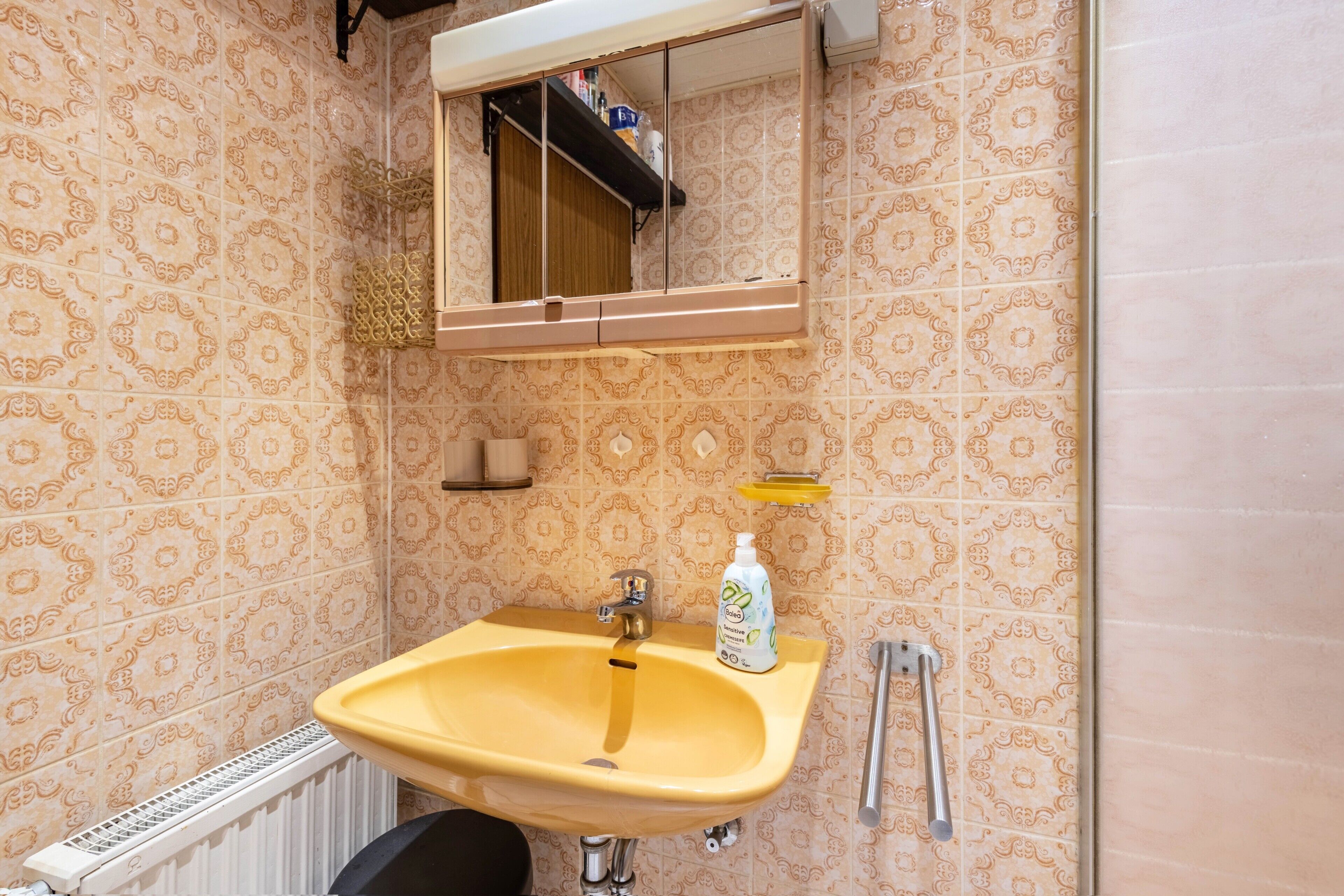 Une salle de bain avec un lavabo jaune, un miroir et des carreaux à motifs.