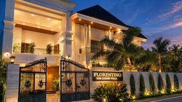 Un edificio grande de dos pisos con entrada protegida por una reja, un letrero que dice 'Florentino The Luxury Villa' y una fachada bien iluminada.