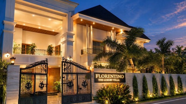 A large, two-story building with a gated entrance, a sign reading 'Florentino The Luxury Villa,' and a well-lit facade.