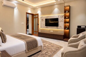 A modern bedroom with a large bed, a TV mounted on a marble wall, a seating area with a sofa, and a decorative cabinet.