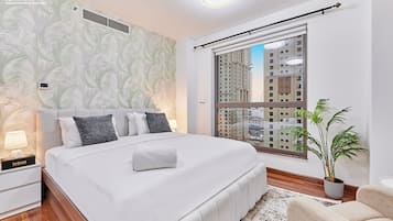 A modern hotel room with a large bed, a nightstand, a potted plant, and a view of tall buildings.