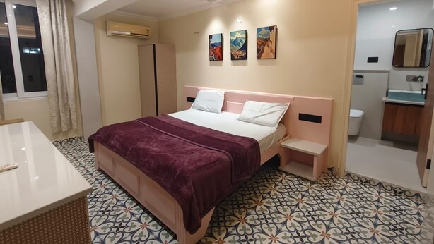 Habitación de hotel con cama, mesitas de noche, escritorio, aire acondicionado, baño y ventana con cortinas.