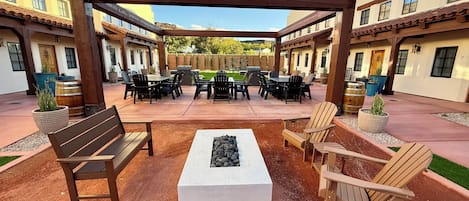 Ein Außenbereich mit einer Holz-Pergola, Sitzgelegenheiten und einer Feuerstelle.