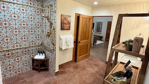 A bathroom with a shower, a wooden door, a towel rack, and a shelf with toiletries. - Casa De Hot Springs (La Verkin)