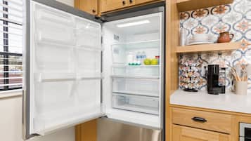 Un refrigerador abierto con estantes transparentes, una cafetera y un protector contra salpicaduras de azulejos.