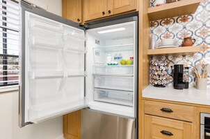 Un refrigerador abierto con estantes transparentes, una cafetera y un protector contra salpicaduras de azulejos.